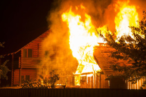 Burning wooden house at night. Bright orange flames and dense sm